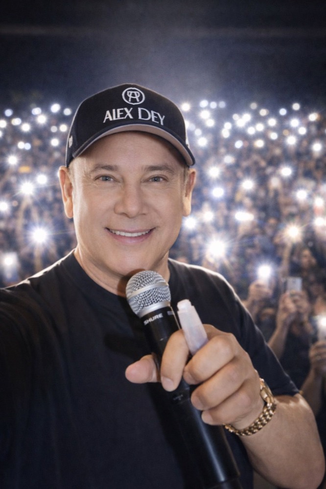 Alex Dey apuntando el micrófono al público, con la audiencia iluminada al fondo